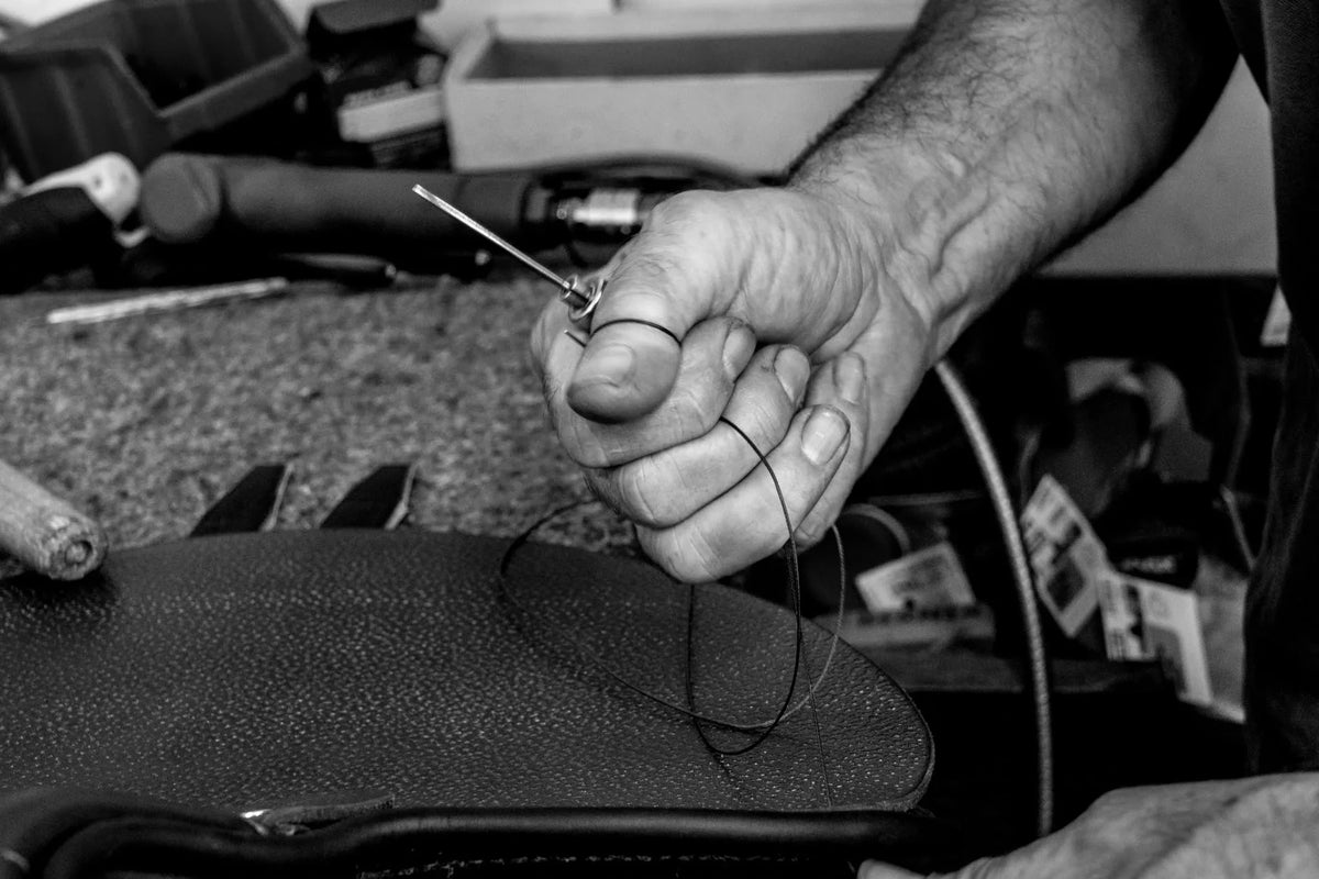 Main d’un artisan cousant une pièce de cuir à la Sellerie Cassou